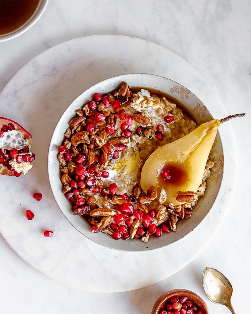 soaked oatmeal porridge in white bowl garnished by pomegranate seeds, pecans and pears