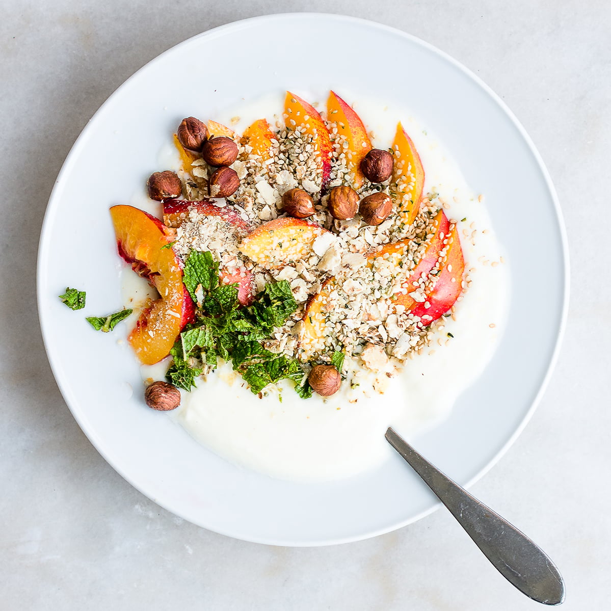 Bowl of homemade yogurt garnished with nectarines, mint, hemp seeds and almonds