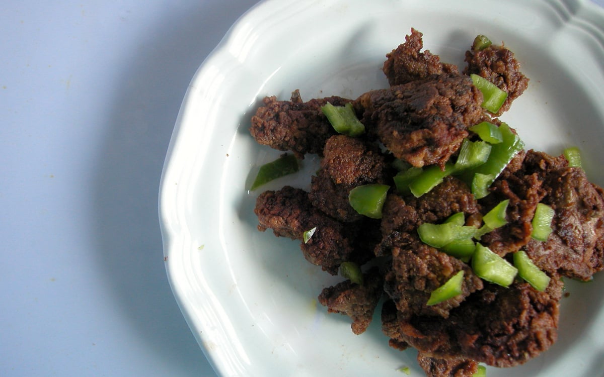 fried chicken livers garnished with chopped green chiles on a white plate