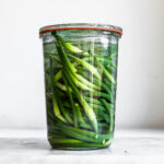 Garlic scapes in clear glass jar on plain background