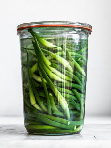 Garlic scapes in clear glass jar on plain background