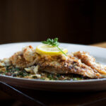 Sole meuniere garnished with lemon and parsley on white plate with dark background