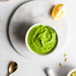 Mustard green pesto in a white bowl on a marble surface