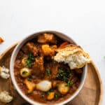 beef and bacon stew served with a crusty piece of bread in a white bowl