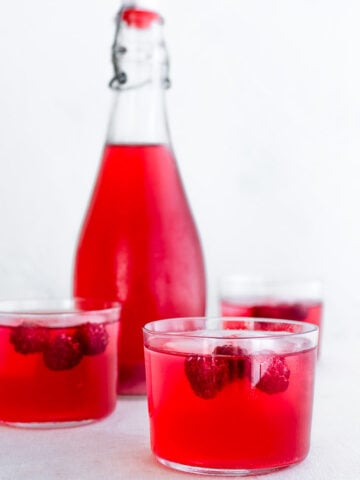 three glasses and a bottle containing raspberry soda and ice