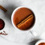 mayan hot chocolate in a white mug on a marble surface, garnished with cinnamon and annatto.