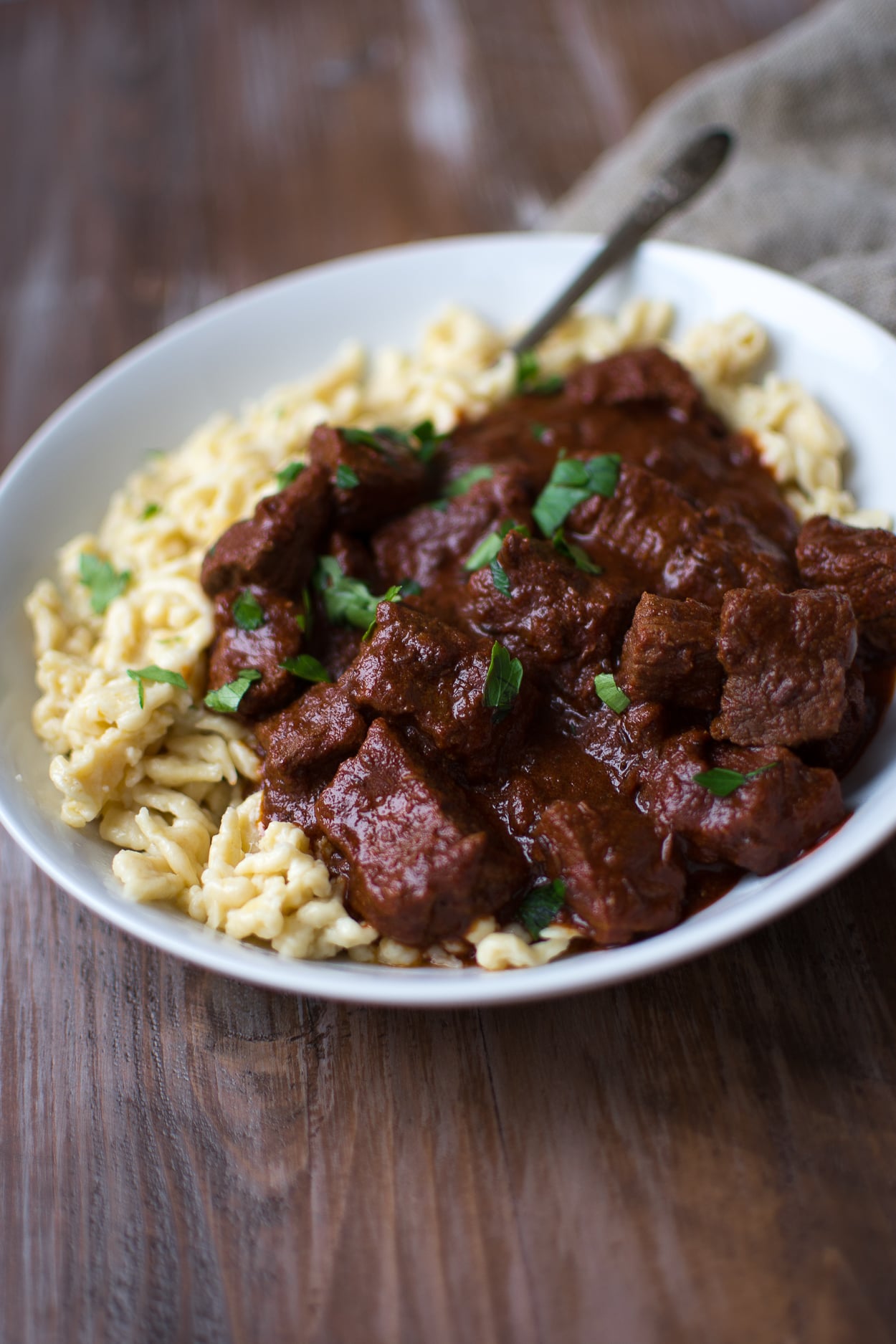 German goulash served over spatsle in a white bowl on a wooden background