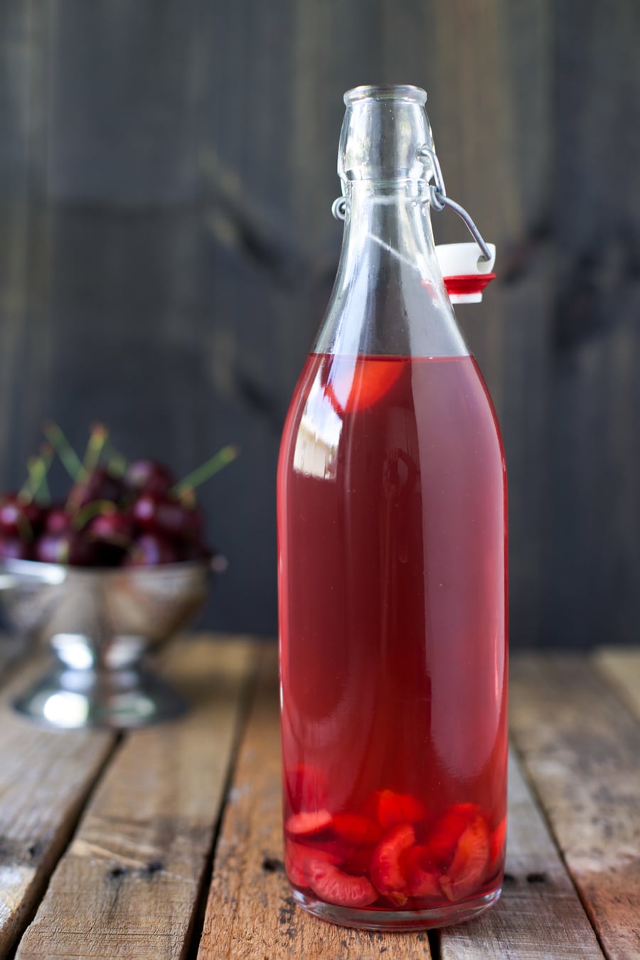 Cherry water kefir in a glass bottle, surrounded by sweet cherries.