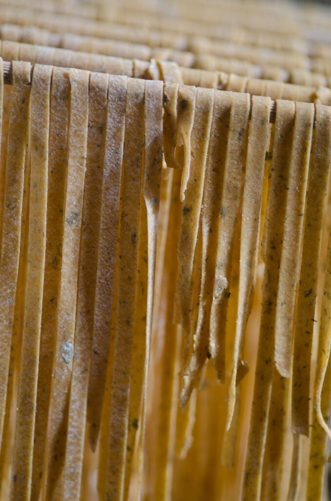 sourdough noodles with herbs drying on a rack