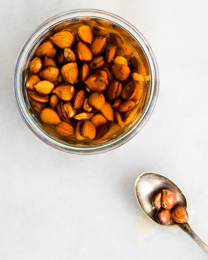 Apricot kernels sit in a glass jar of noyaux (homemade almond extract).