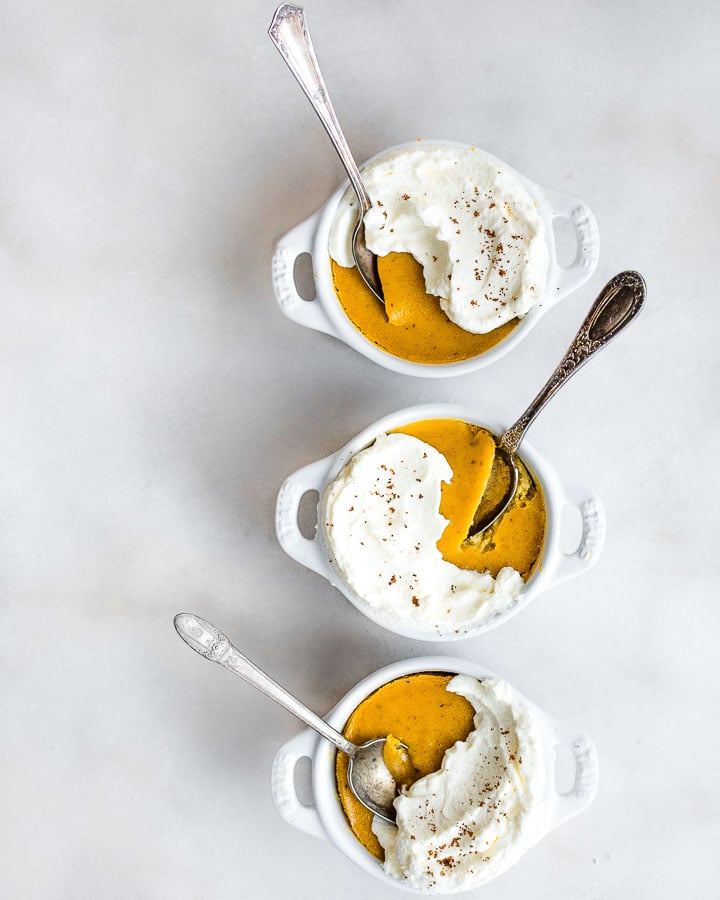 Three ramekins filled with pumpkin custard and topped with whipped cream.