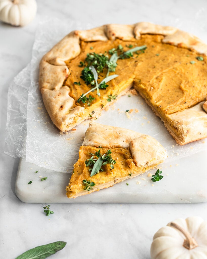 Pumpkin galette garnished with sage and thyme on a piece of white parchment paper.