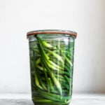 Garlic scapes in clear glass jar on plain background