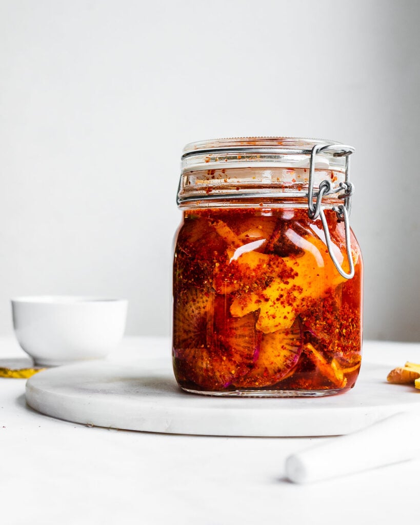 Daikon radish kimchi in a Fido jar on a white surface.