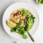 Ginger and chicken soup in a white bowl garnished with cilantro, chili pepper, scallions and lime