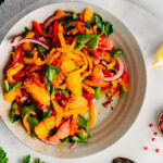 Bell Pepper Salad on an earthenware plate next to a lemon wedge and pinch bowl filled with pink peppercorns