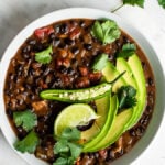 Black bean soup with chicken in a bowl, garnished with cilantro, lime, avocado and serrano chili
