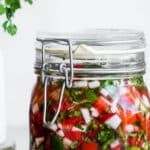 fermented salsa in a glass jar, garnished with cilantro flowers and lime