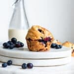 Einkorn blueberry muffins on white surface with blueberries and milk in the background