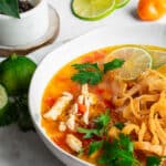 Lime soup in white bowl, garnished with cilantro, habanero peppers and lime