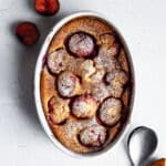 Plum clafoutis in white casserole dish on white surface