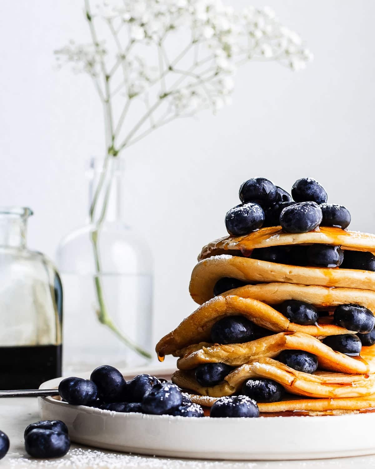 Stack of einkorn pancakes garnished with blueberries and drizzled with maple syrup on white plate.