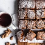 Einkorn gingerbread on a wooden surface next to a mug of tea, fresh ginger in background