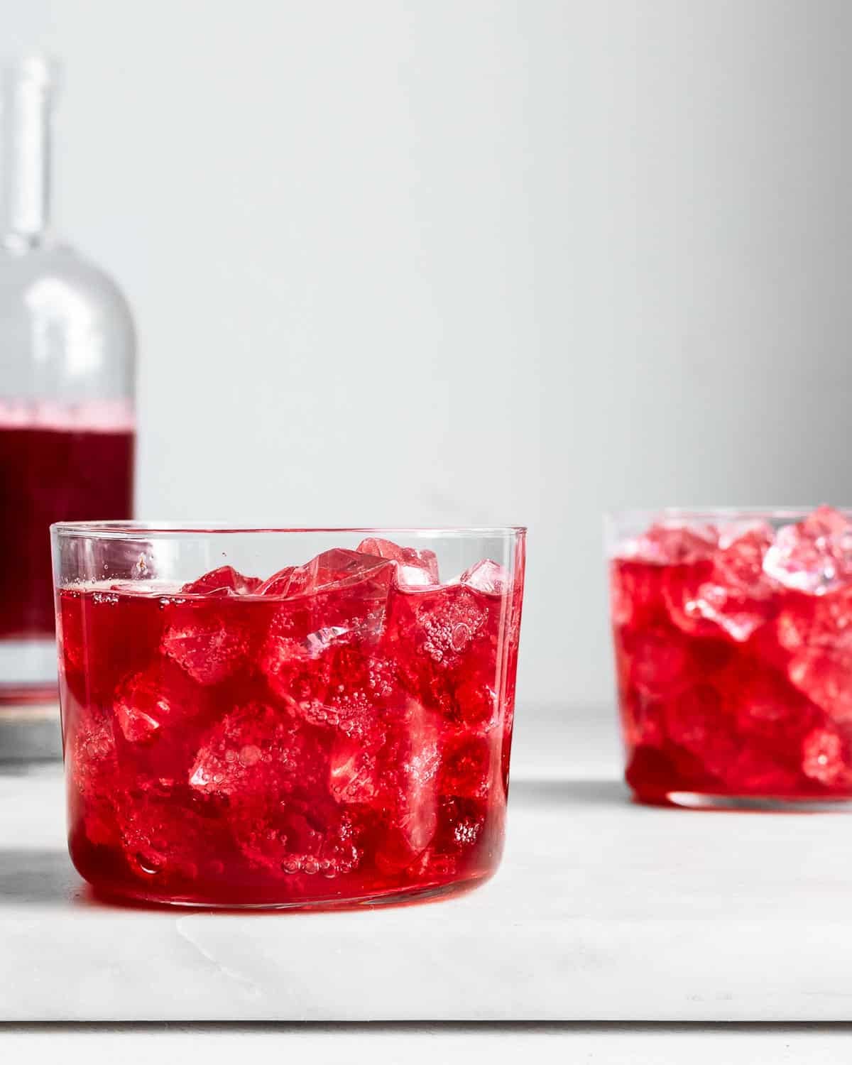 hibiscus kombucha in a glass with ice, more hibiscus kombucha in a bottle in the background