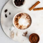 chocolate tea latte in a white mug on a marble surface, garnished with cacao nibs and cinnamon