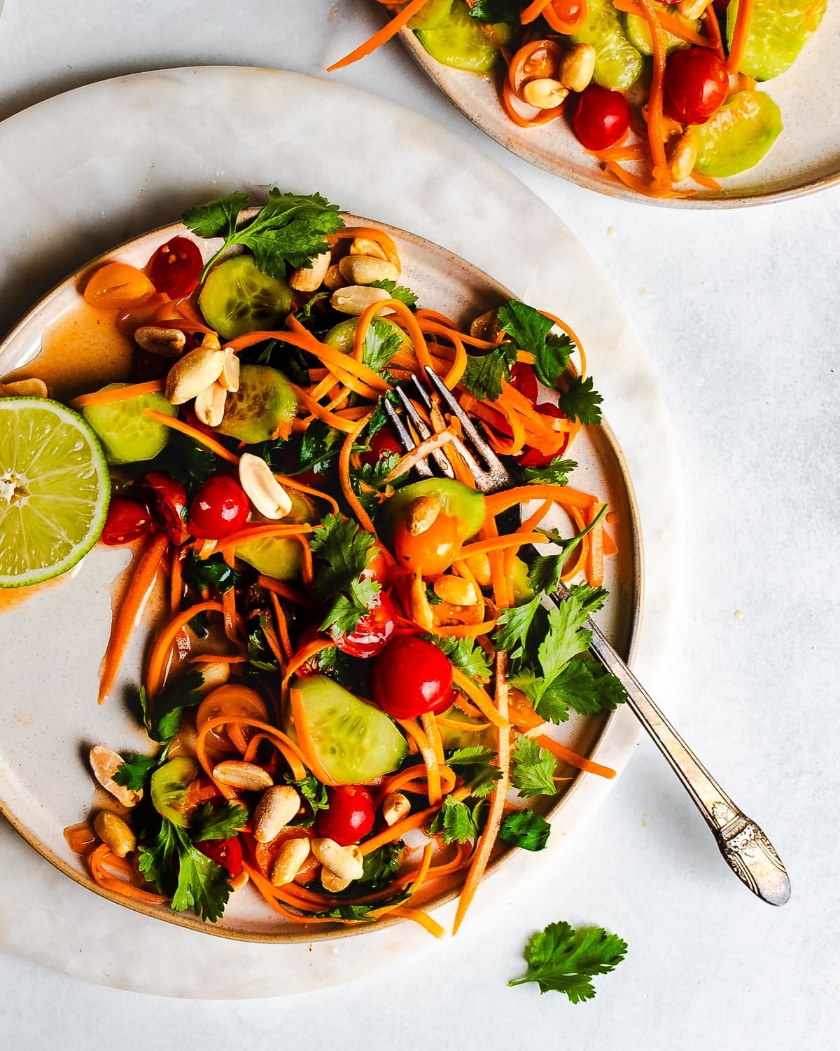 Thai salad with carrots, tomatoes, cucumbers, and peanuts on a plate garnished with lime.