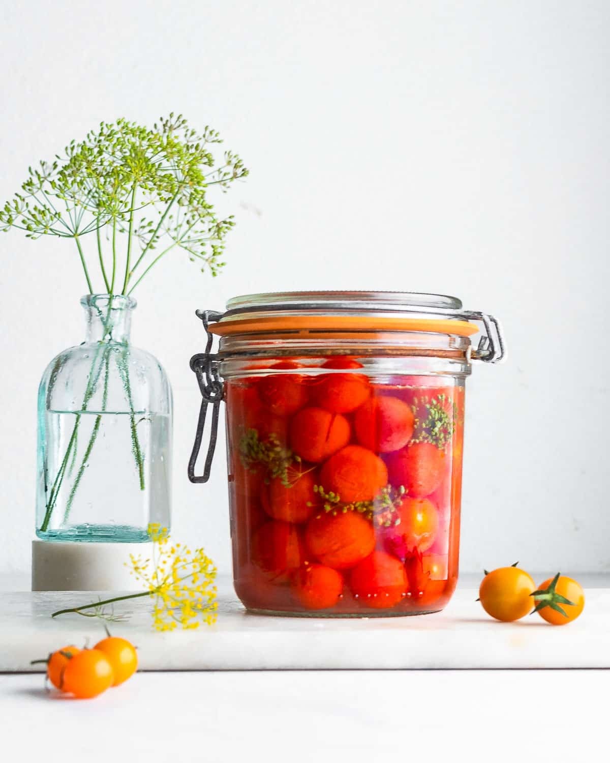 Fermented cherry tomatoes in a clip-top jar, with dill flowers in the background