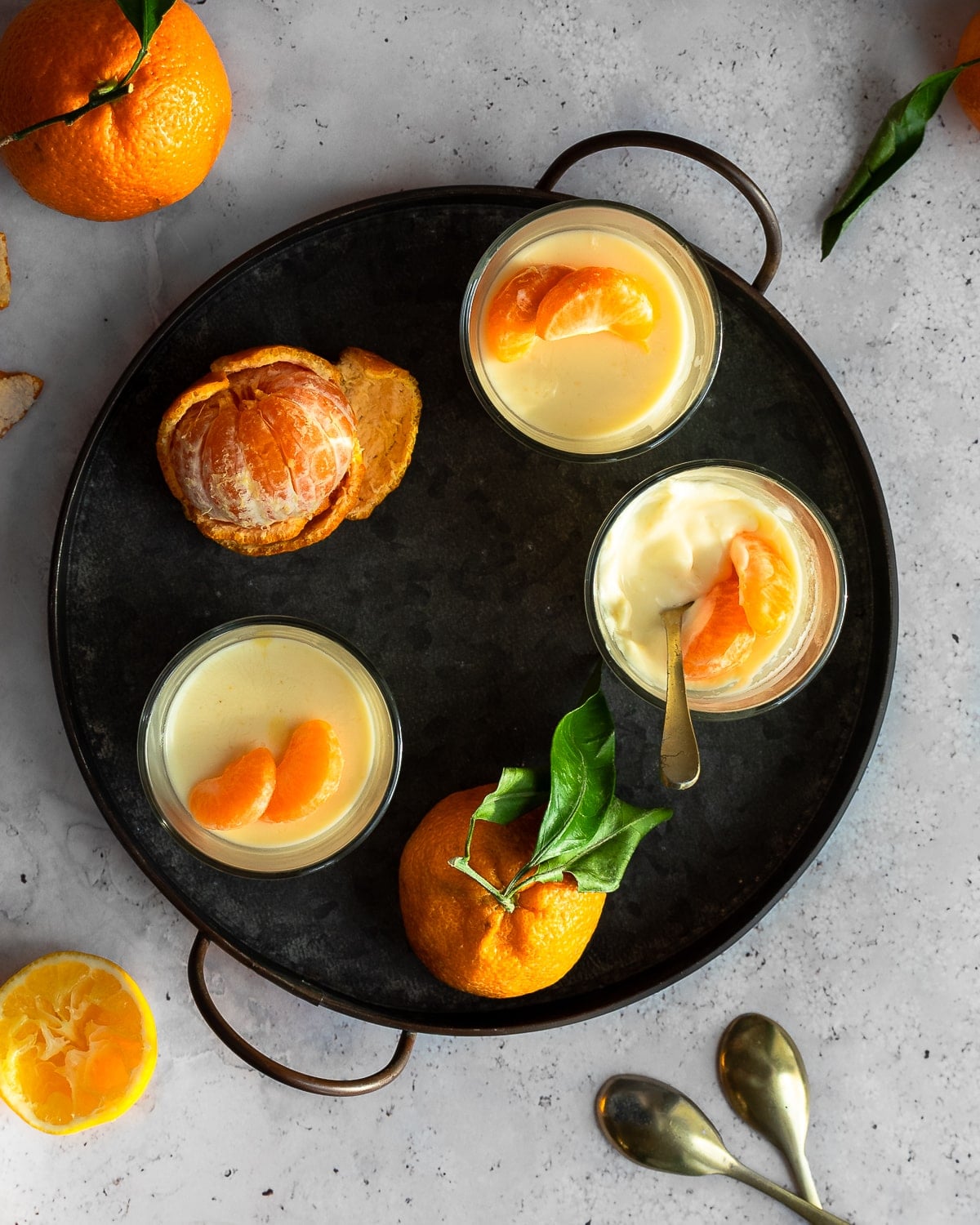 Three citrus-honey possets on a metal tray, garnished with satsuma orange segments.