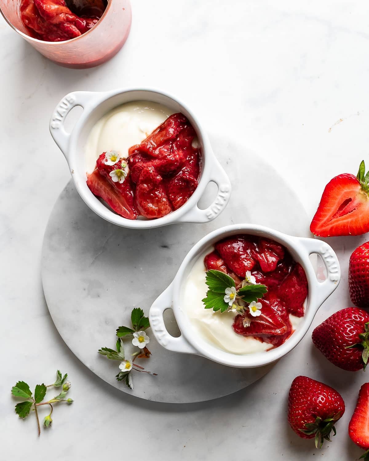 roasted strawberries spooned over yogurt on a marble surface, decorated with strawberry flowers