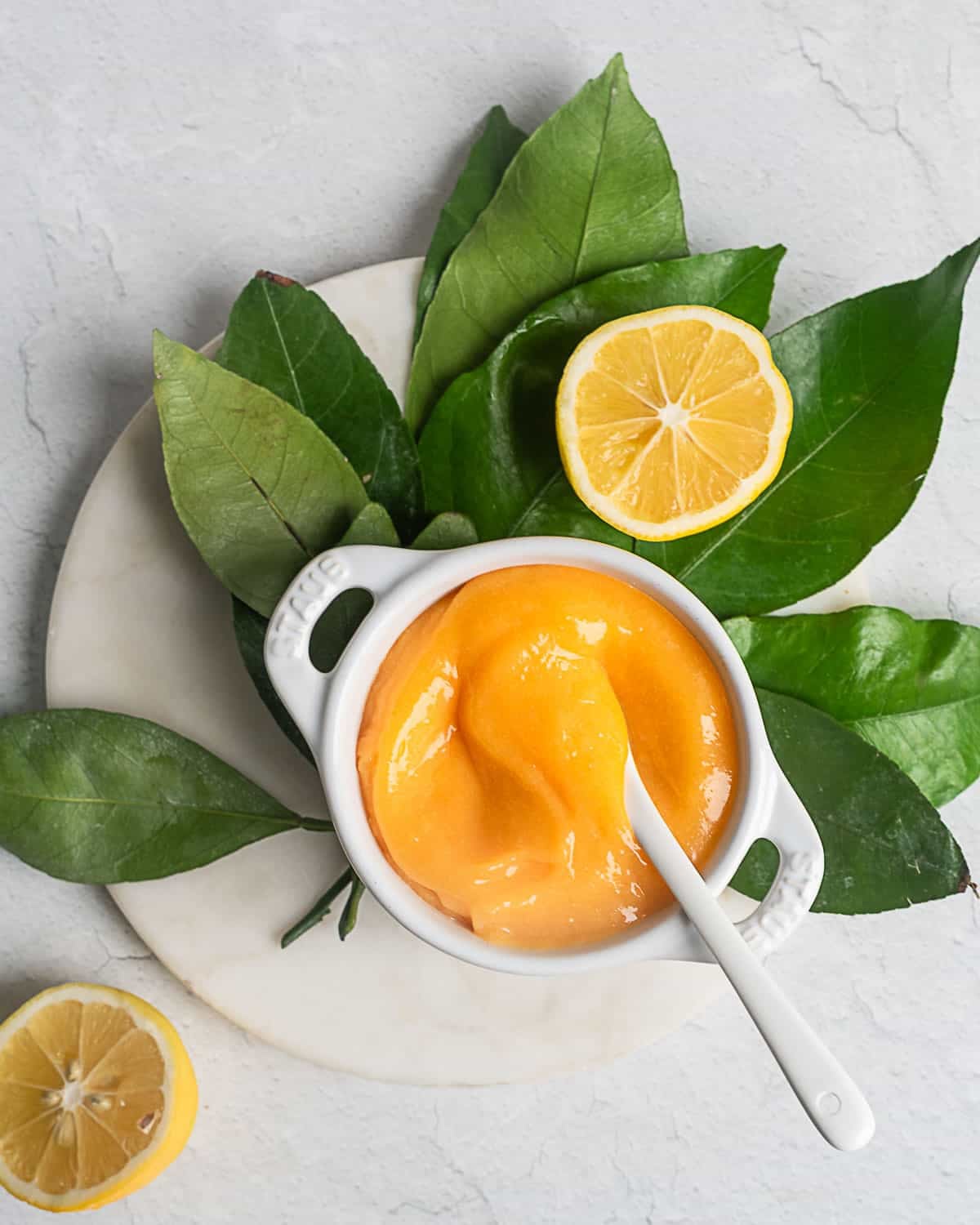 Lemon curd in a white ramekin nestled on top of citrus leaves